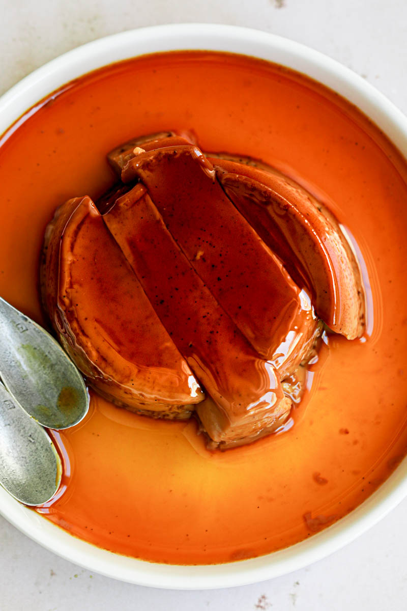 A closeup of one dulce de leche flan sliced, with a spoon on the side.