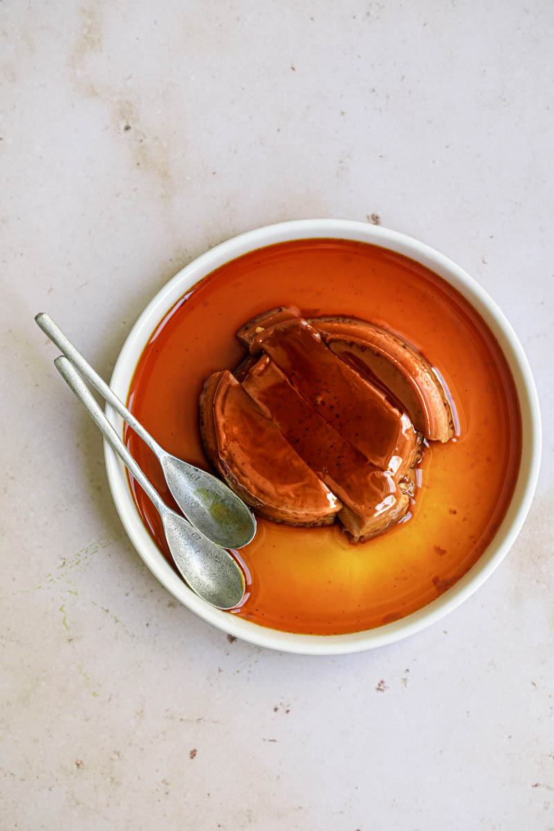 One dulce de leche flan sliced, on a white plate, with a spoon on the side.