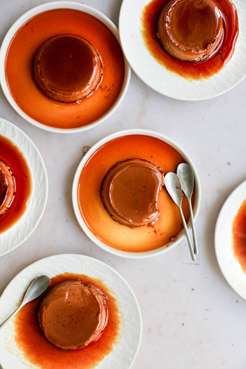 The mini-individual dulce de leche flan on white plates arranged in an irregular manner, as seen from above.