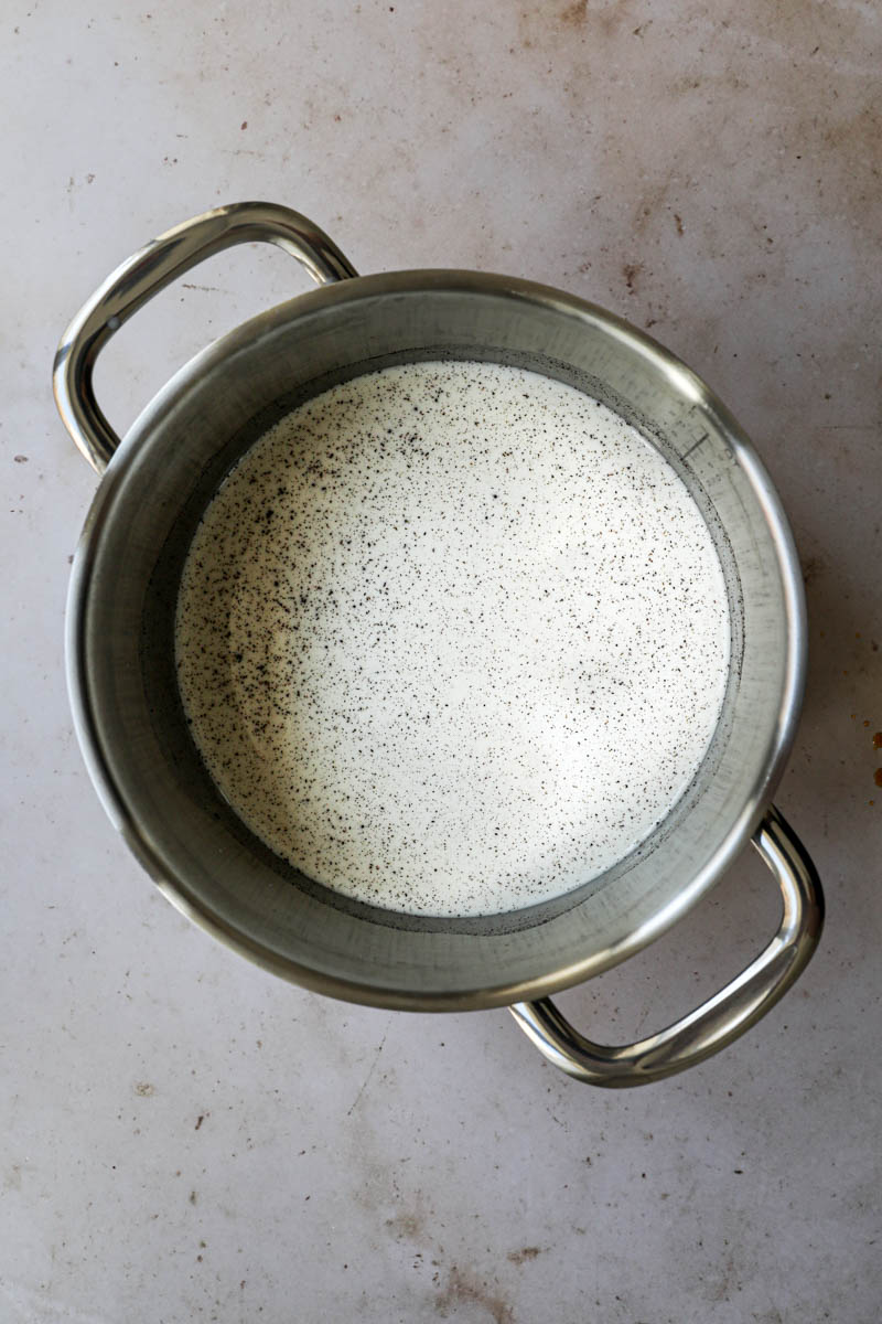 Preparing the dulce de leche flan batter: a large pot filled with milk, scrapped vanilla bean and sugar.