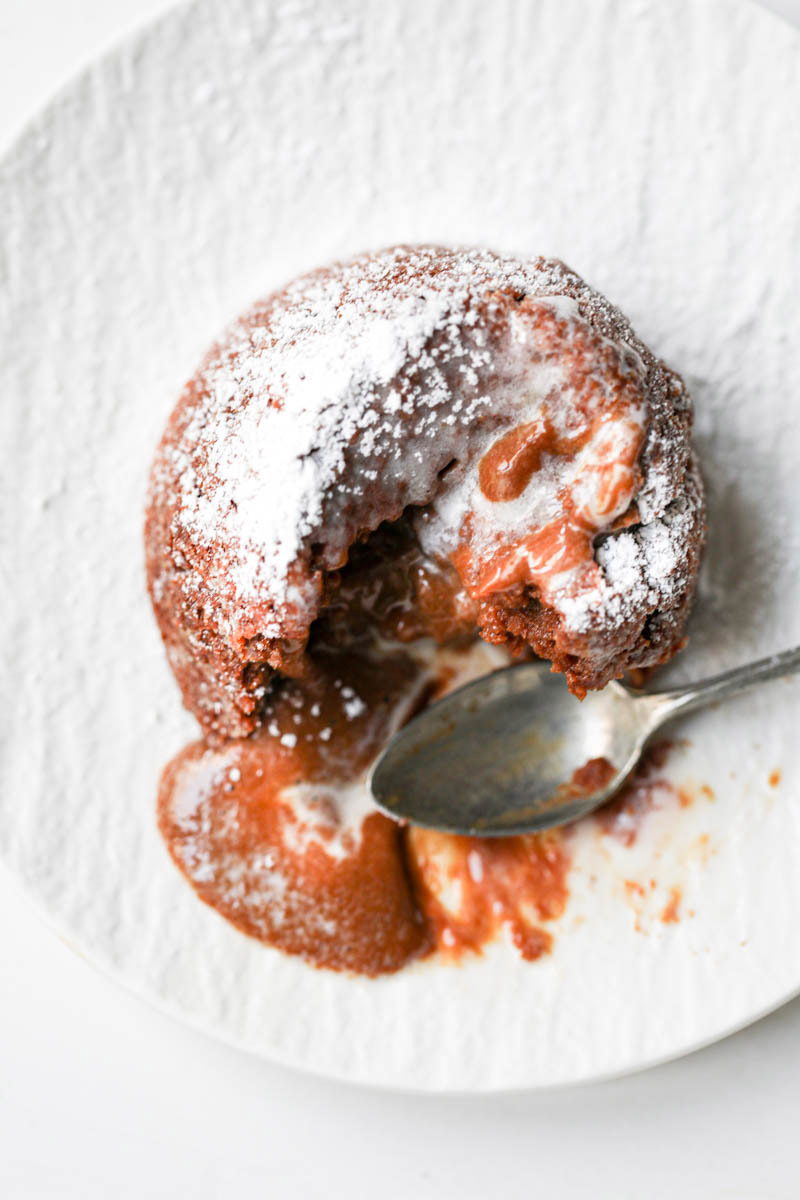 Closeup of the dulce de leche lava cake with a scoop of melted ice cream and a spoon on the side seen from above.