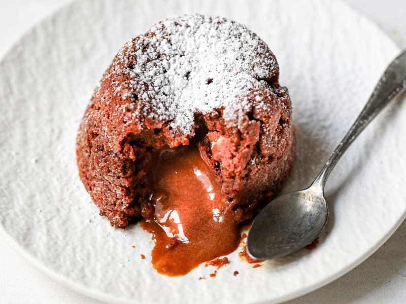 Closeup of dulce de leche lava cake on a white plate with spoon on the side.