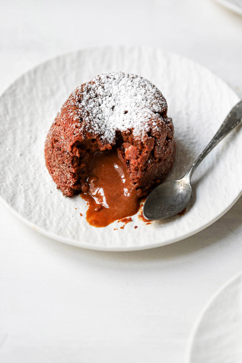 Closeup of dulce de leche lava cake on a white plate with spoon on the side.