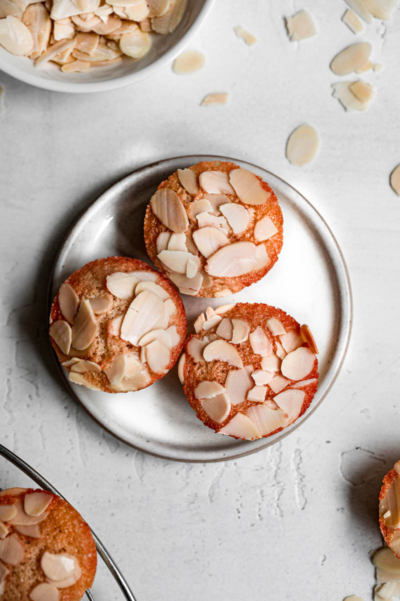 Three small financier cake on a small white plate and a part of a wire rack in the bottom left corner.