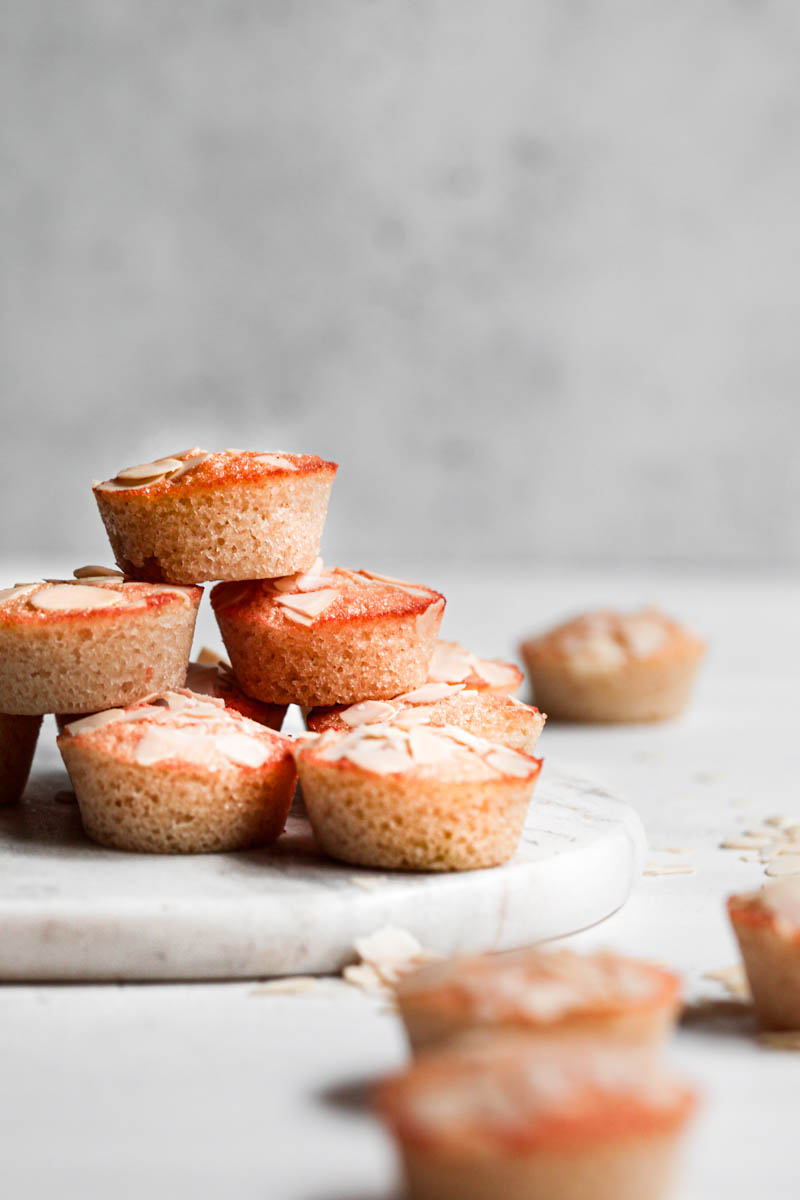 Stacked almond financier cakes on top of marble platter with some small financiers around it.