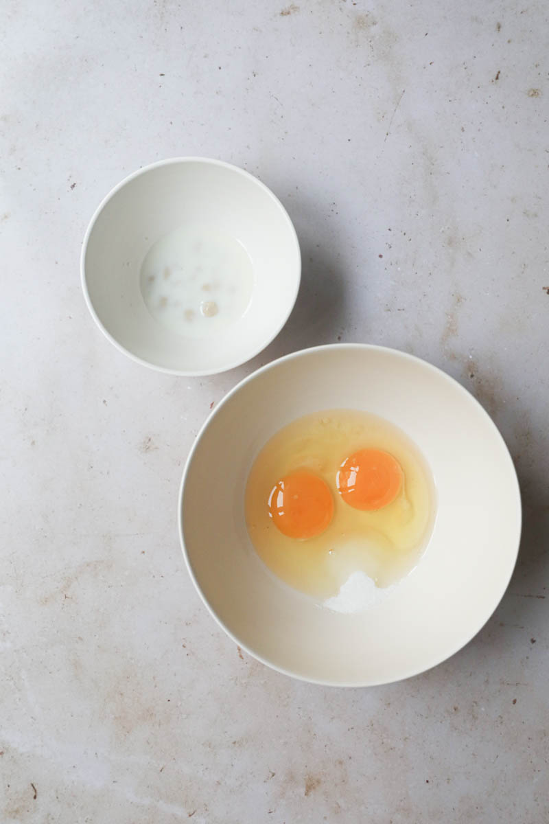 The eggs and sugar in a bowl and the milk and yeast on another bowl next to it.