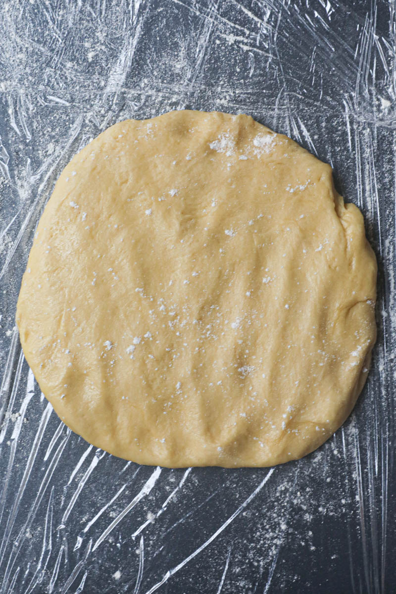 The French brioche bread dough flattened out on top of a baking tray lined with saran wrap.