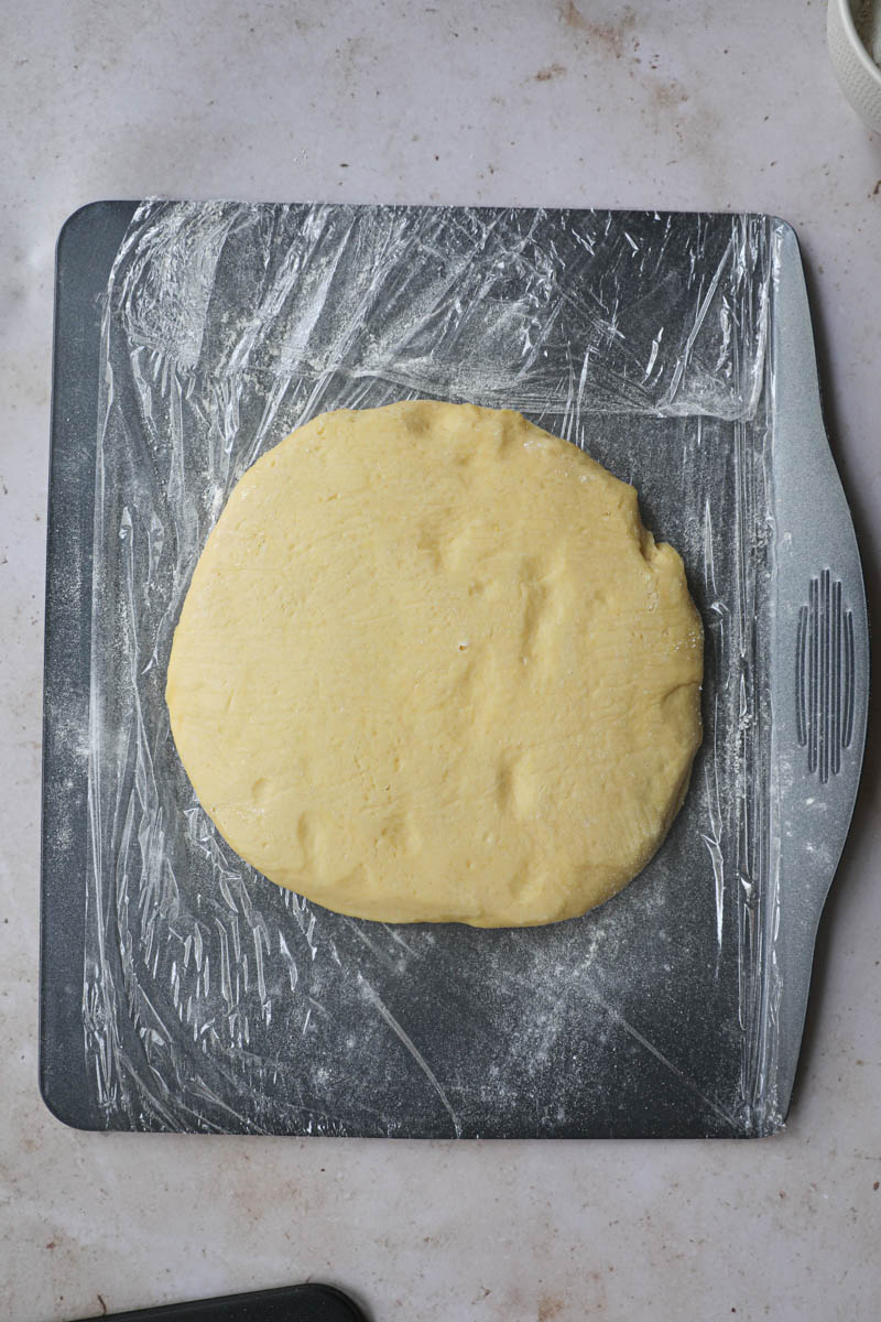 The French brioche bread dough flattened out on top of a baking tray lined with saran wrap after 24 hours in the refrigerator.