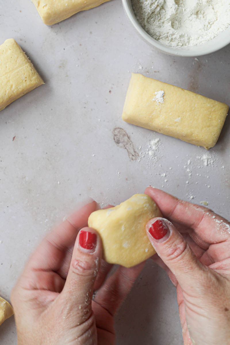 2 Hands shaping one piece of brioche bread dough into a tight ball with other pieces of dough around.