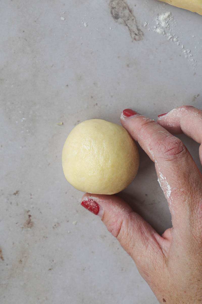 One hand holding one piece of brioche bread dough shaped into a tight ball.