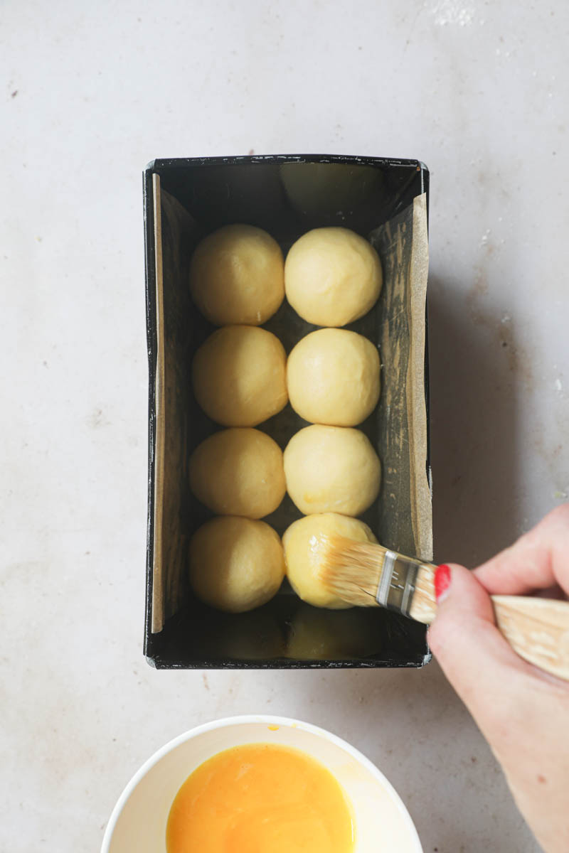 One hand brushing the brioche with egg wash.