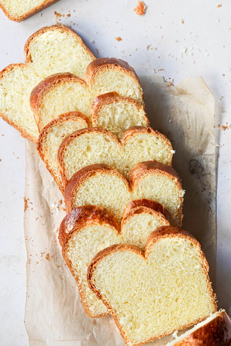 The whole brioche loaf bread sliced on top of a piece of parchment paper.