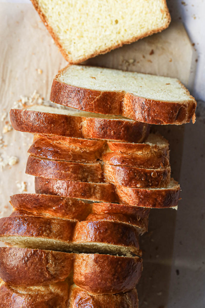 The whole brioche loaf bread sliced on top of a piece of parchment paper as seen from above.