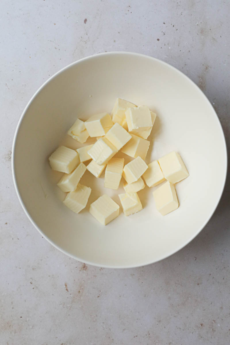 The pieces of butter cut in small cubes inside a beige bowl.