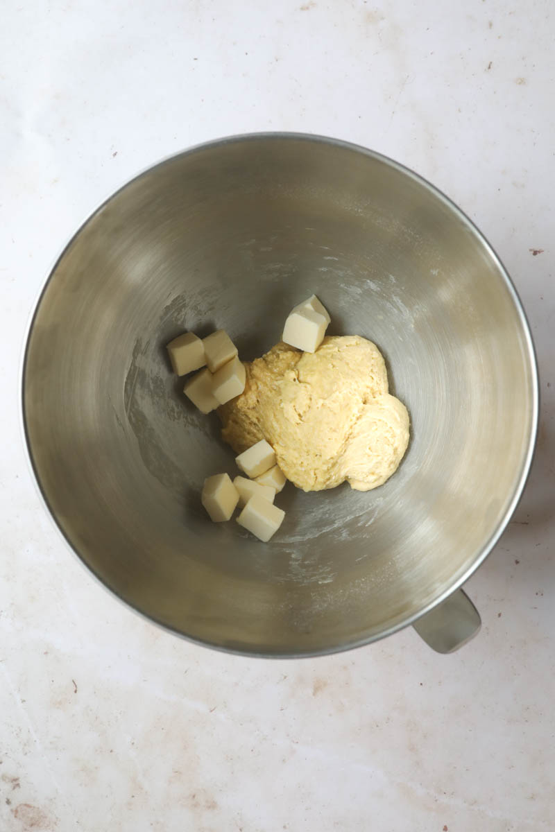 The brioche bread dough with half the butter inside a mixing bowl.