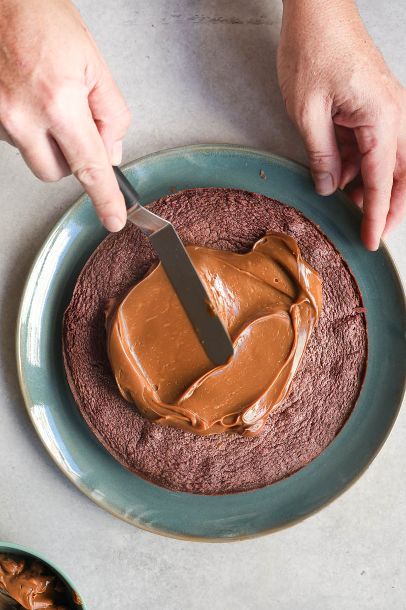 One hand spreading a layer of dulce de leche over the French chocolate cake with a small off set spatula.