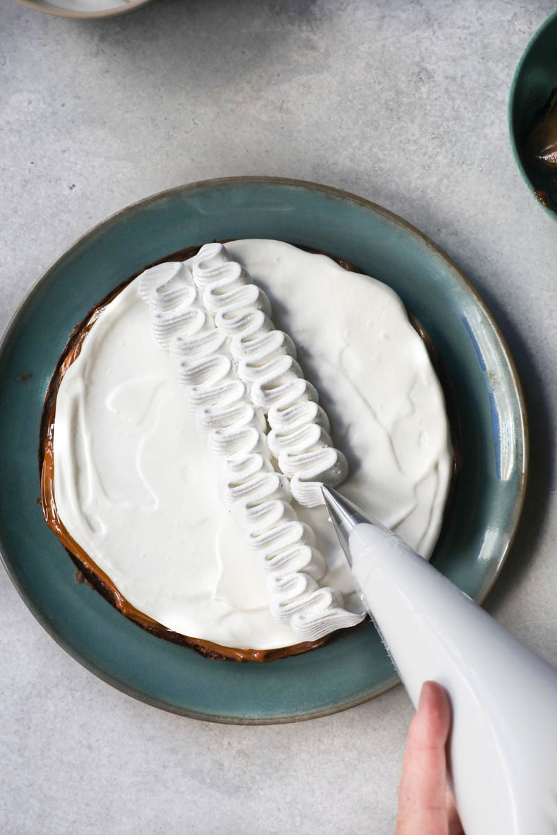 2 Hands holding a piping bag decorating the French chocolate cake.