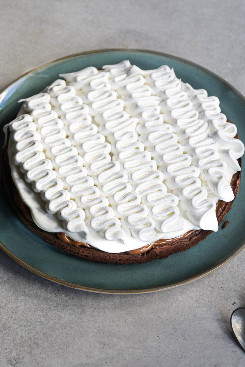 The whole French chocolate cake filled with whipped cream and meringue on a blue plate with 2 spoons seen on the bottom right corner.