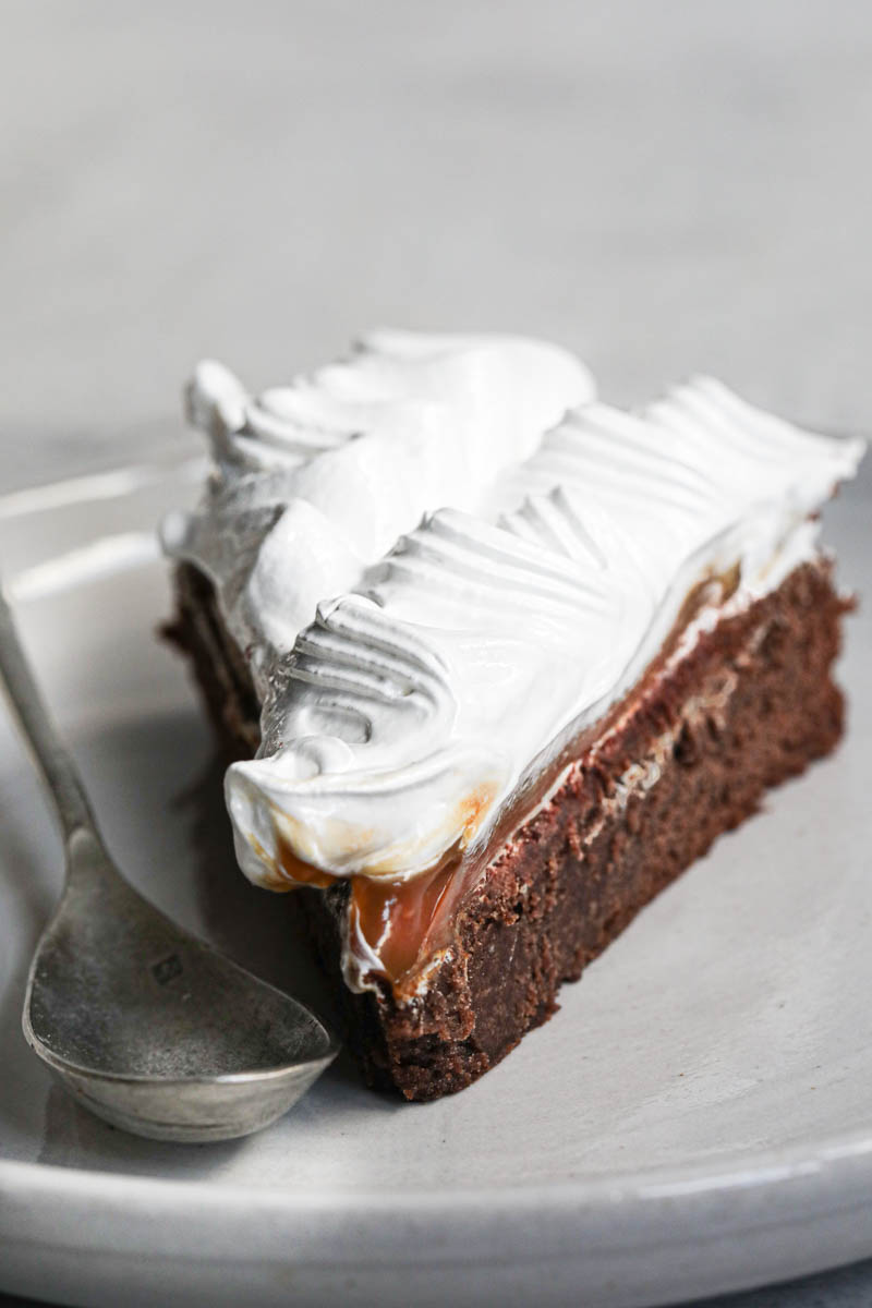 One slice of French chocolate cake filled with whipped cream and meringue on a grey plate with a spoon on the side.