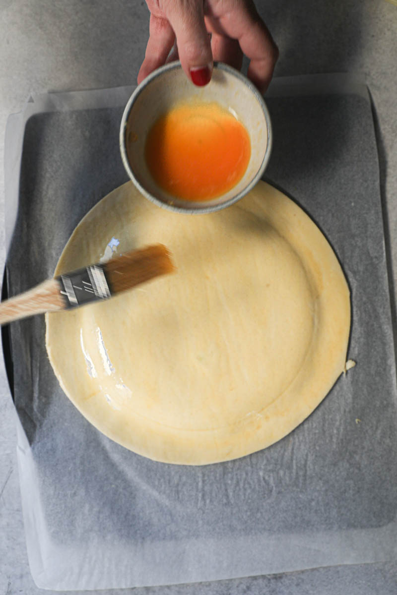 One hand brushing the French king cake with egg wash.