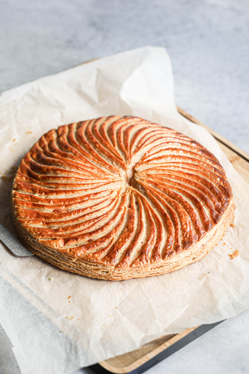 The whole French King cake covered with a piece of parchment paper and a knife on the side.