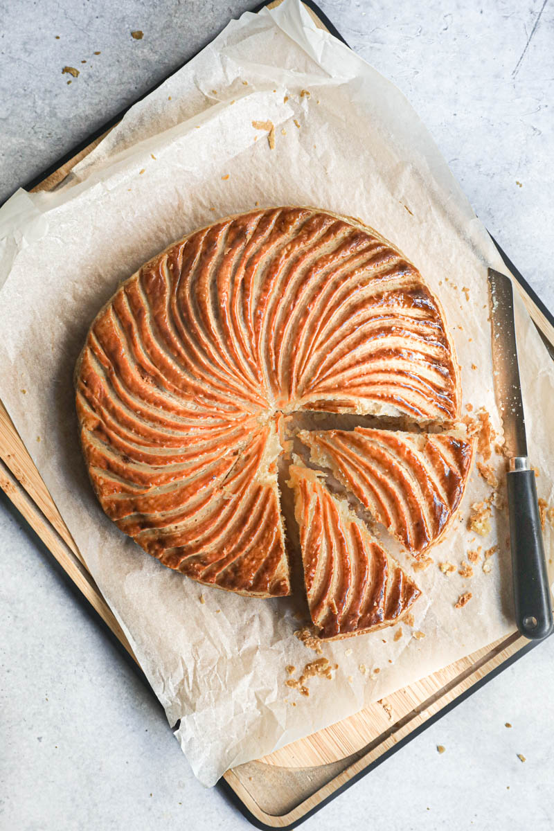 The sliced French King cake seen from above on a wooden board with a knife on the side.