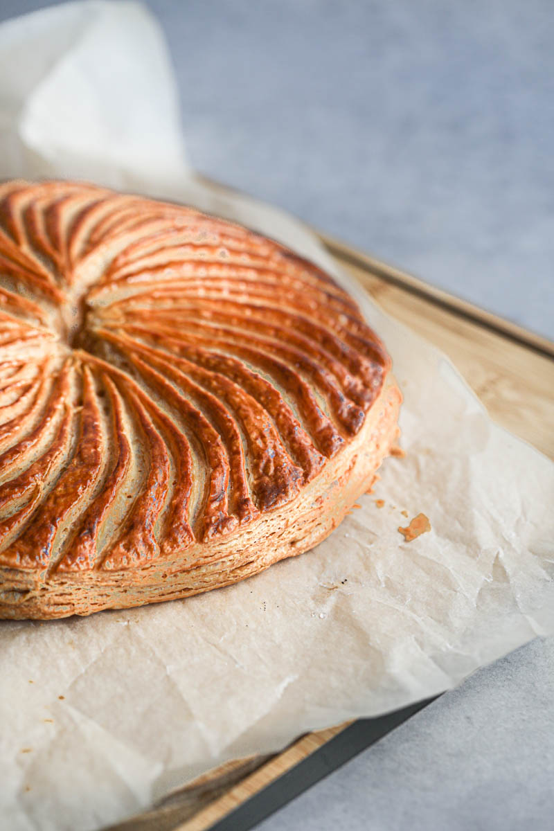 The French king cake on a wooden board covered with a piece of parchment paper and a knife on the side.