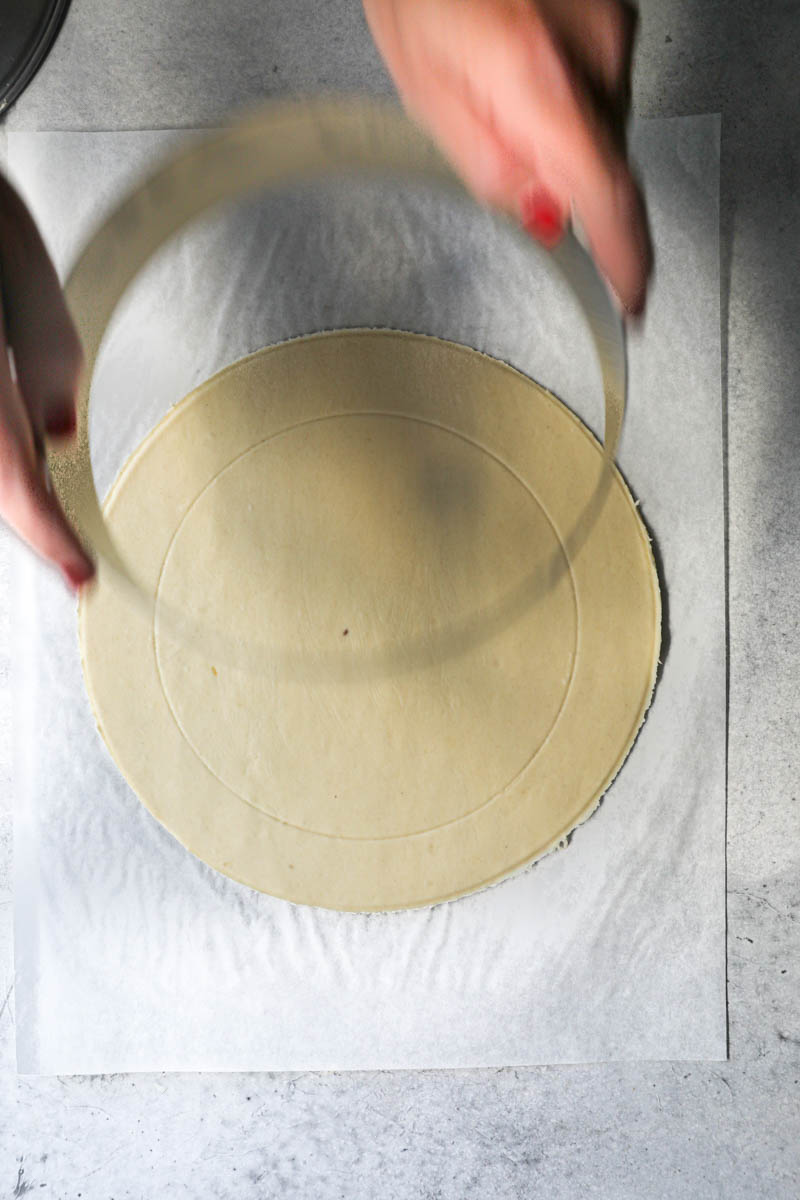 2 hands removing a cake ring from the puff pastry.