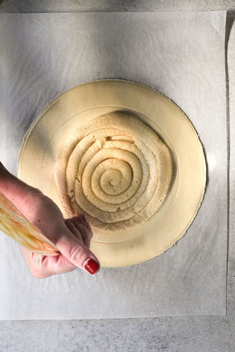 One hand piping the almond cream filling on to the puff pastry round.