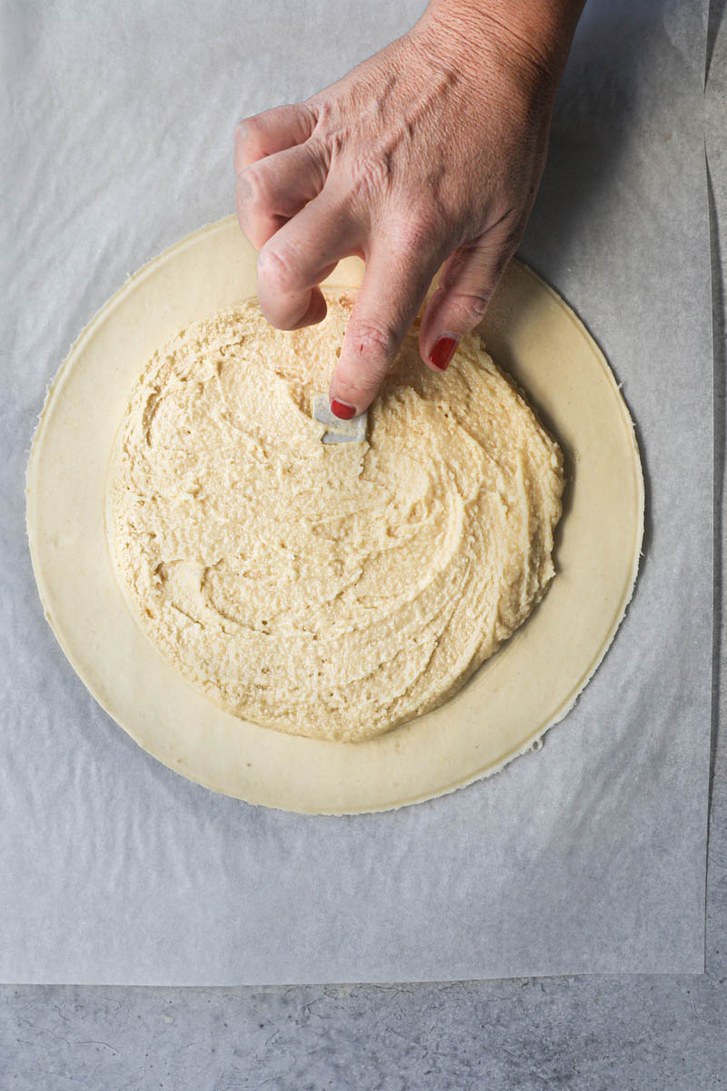 One hand placing the ceramic figurine inside the King cake.