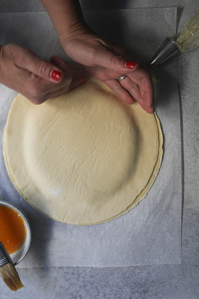 Two hands covering the King cake with the second puff pastry dough disc.