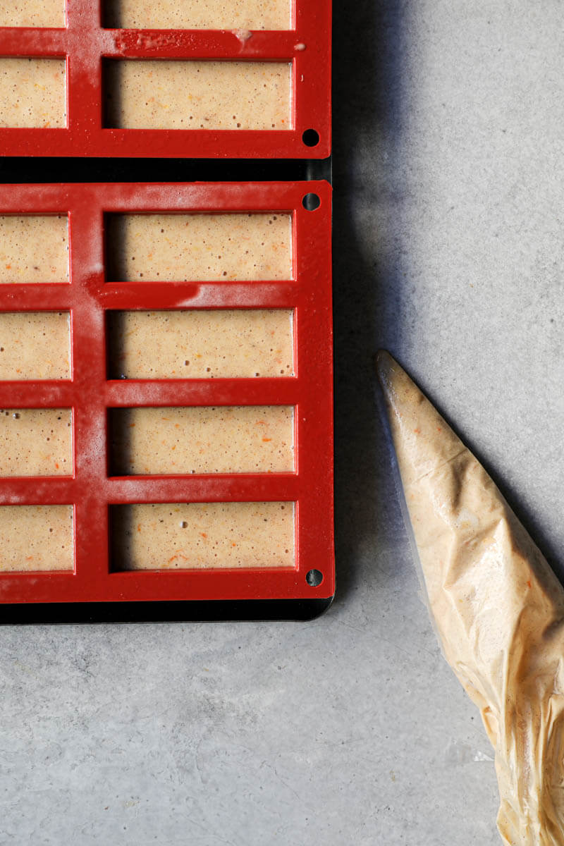 The mini cake molds filled with the pain d'épices batter and a pipping bag next to them.