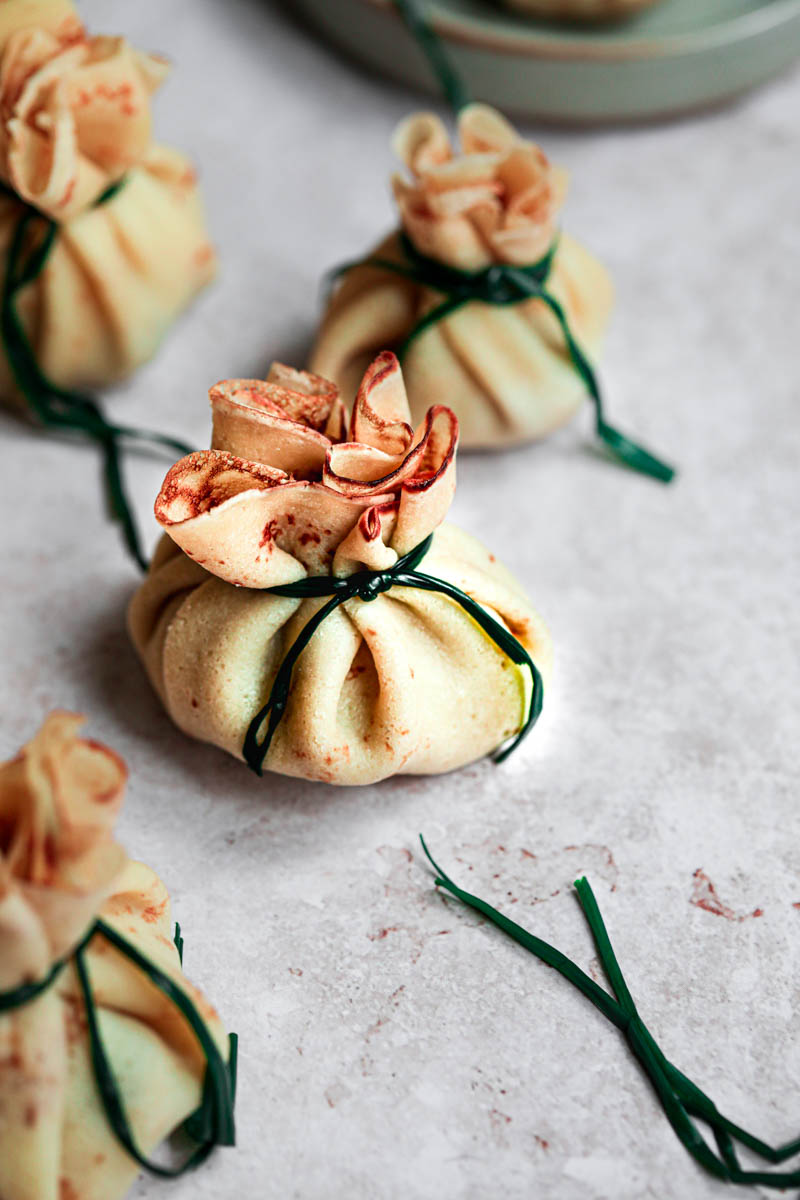 Mushroom and chicken crepes folded as small, wrapped gifts with blanched chives closing them up, as seen from the side.