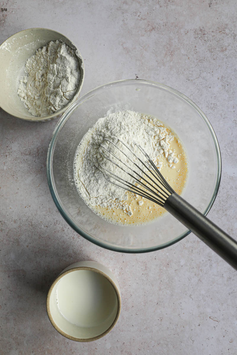 A bowl with the milk, eggs and flour, with a whisk placed inside a bowl, making crepe batter.