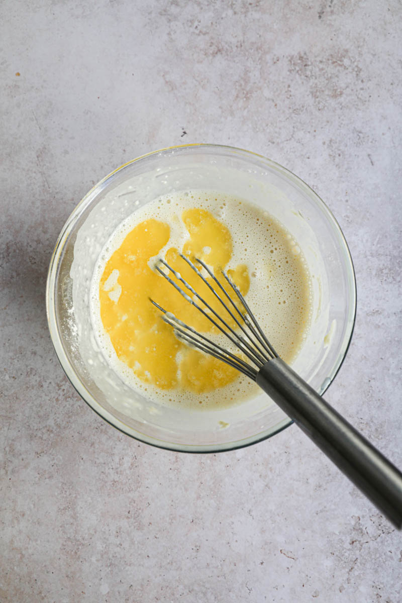 A bowl with the milk, eggs and flour, and the melted butter, making crepe batter.