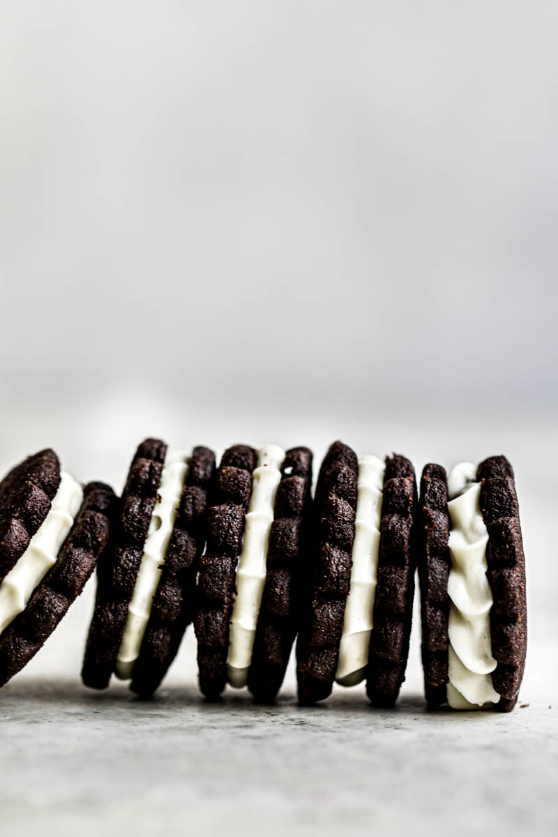 5 homemade Oreo cookies filled with white chocolate cream filling standing next to each other in the bottom part of the frame.