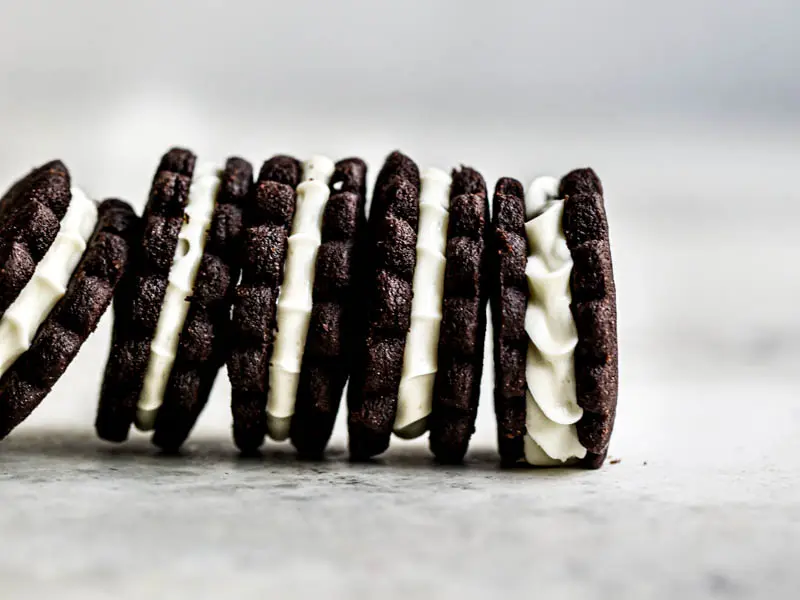 5 homemade Oreo cookies filled with white chocolate cream filling standing next to each other in the bottom part of the frame.