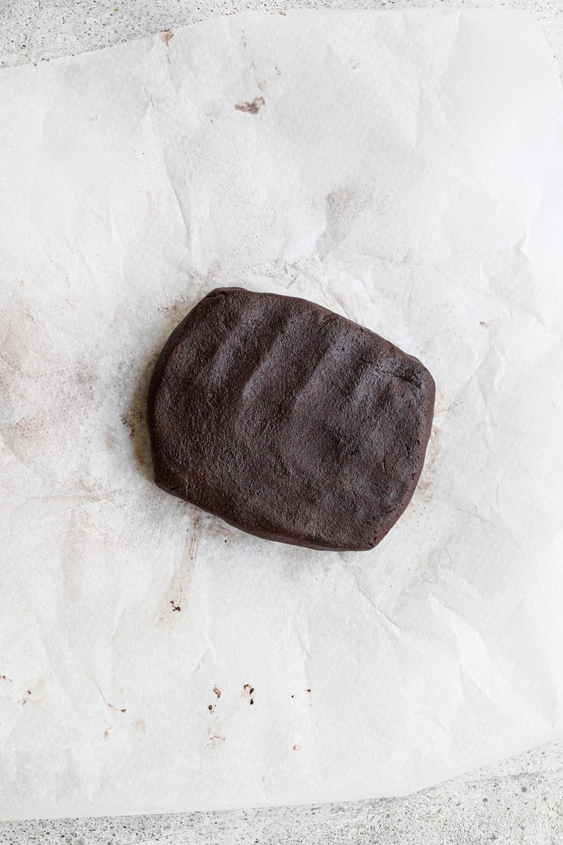 Making the homemade Oreo cookie dough: the Oreo cookie dough shaped into a rectangle on top of a piece of parchment paper.