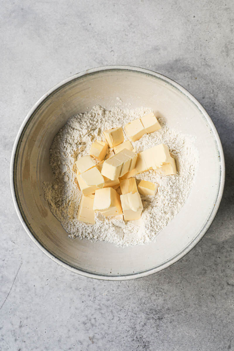 Butter cut in cubes and flour inside a grey ceramic bowl.