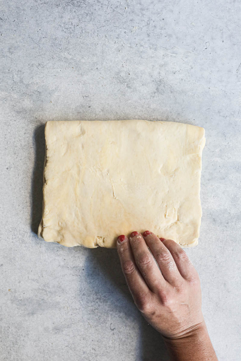 One hand folding the rough puff pastry being over itself as a letter.