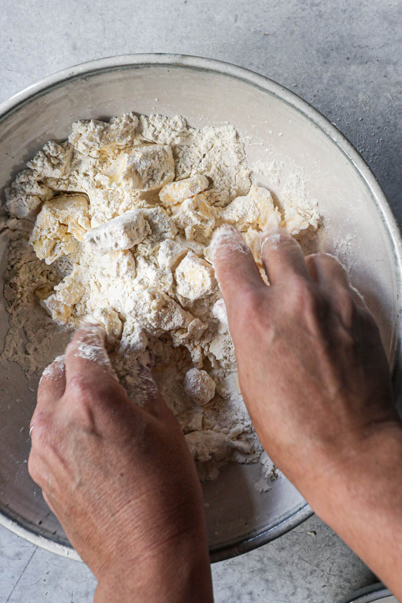 2 Hands breaking the butter apart inside a bowl.