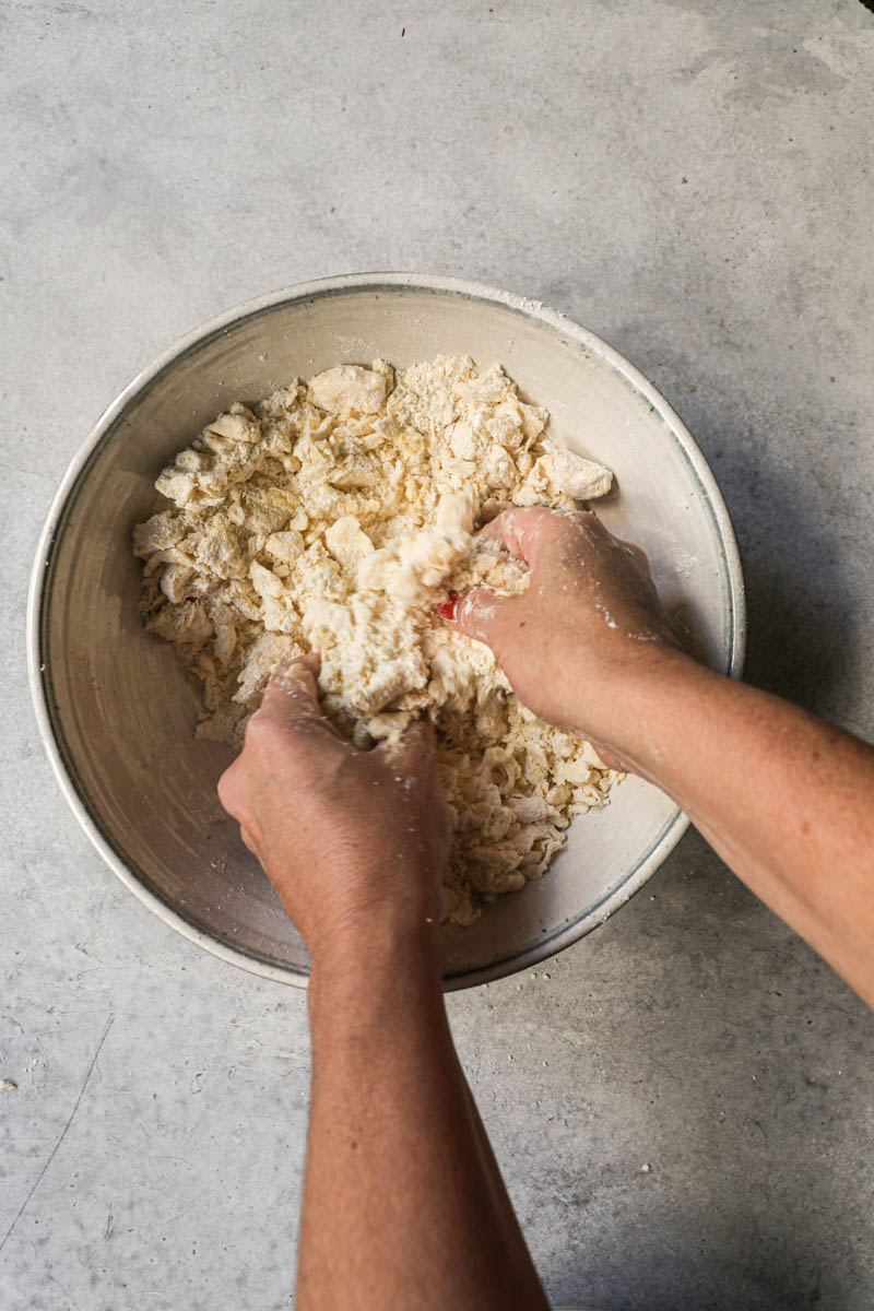 2 Hands breaking the butter apart inside a bowl.