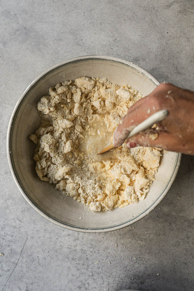 One hand mixing the rough puff pastry dough with a white spatula.