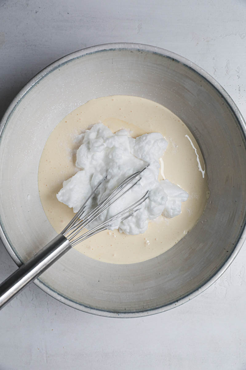 The egg yolks and sugar blanced inside a bowl with one third of the egg whites on top with a whisk inside the bowl.