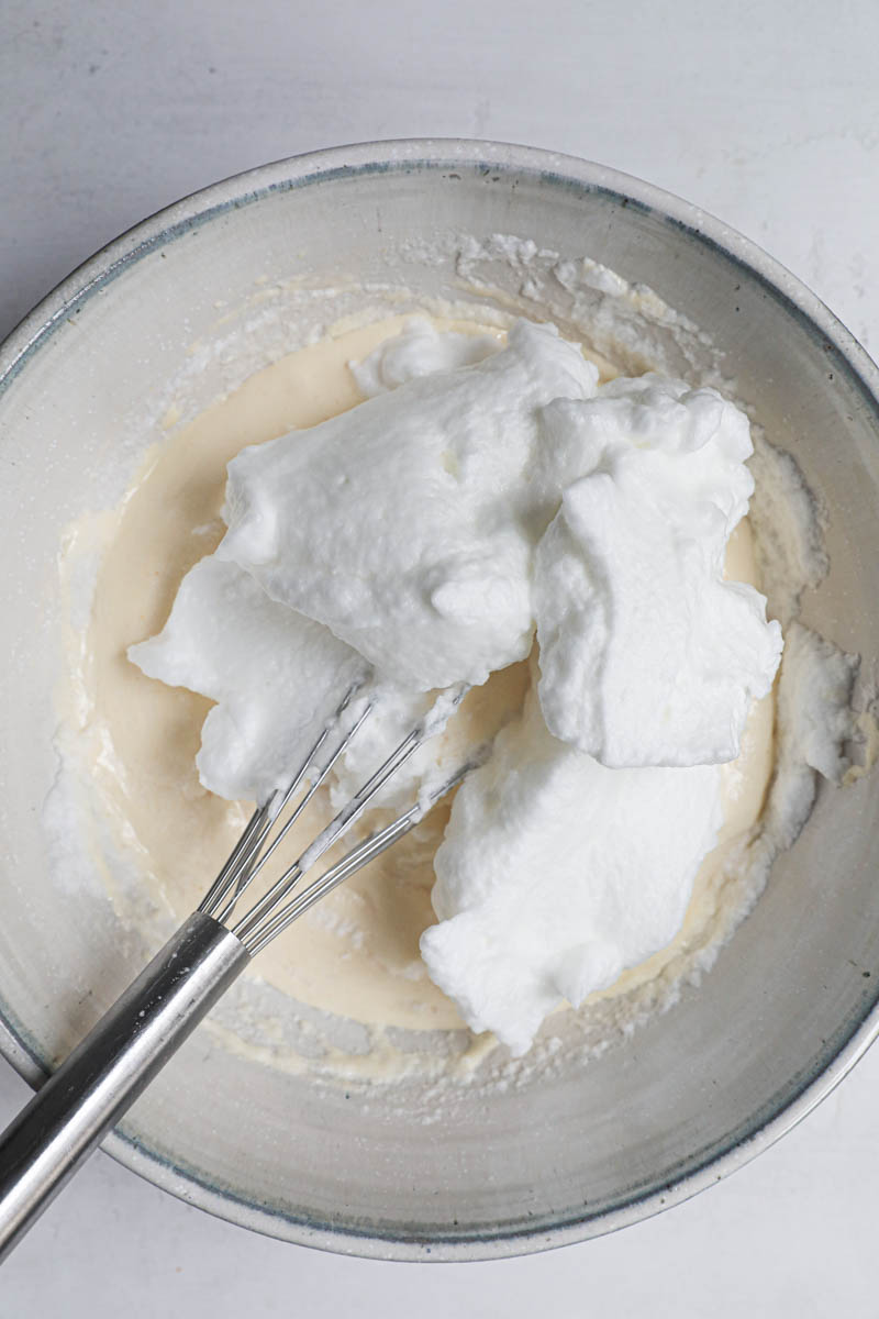 The egg yolks and sugar blanced inside a bowl with the remaining the egg whites on top with a whisk inside the bowl.