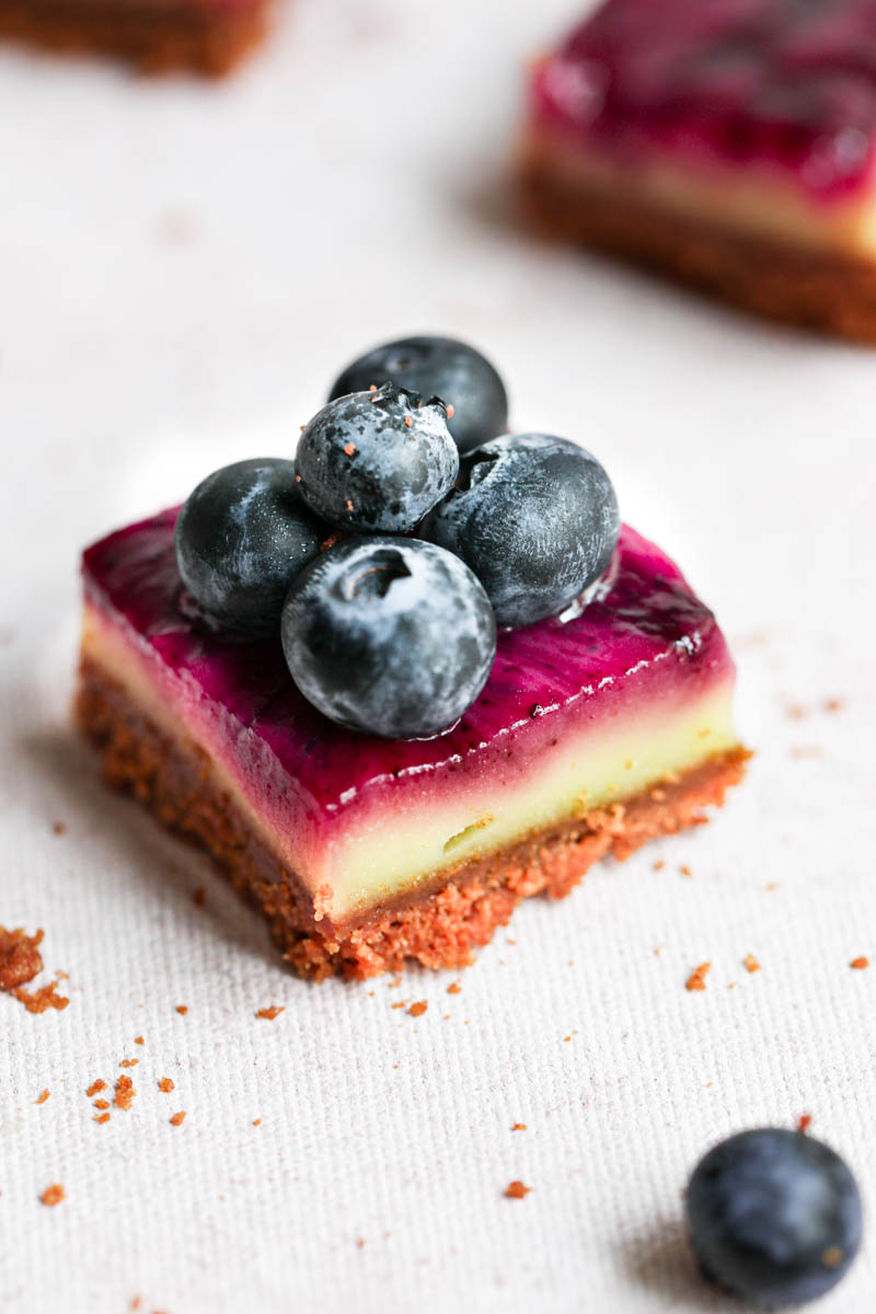 Closeup shot of one creamy square lemon bar with blueberry swirls and blueberries on top.