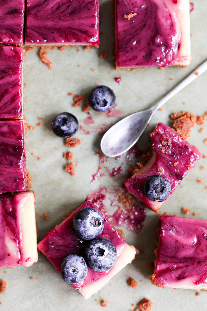 Overhead shot of the sliced lemon bars with one half eaten bar on the side on a baking tray lined with brown parchment paper.