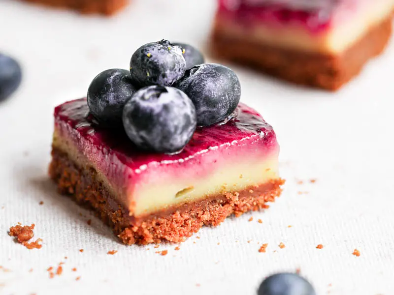 Closeup shot of one creamy square lemon bar with blueberry swirls and blueberries on top.