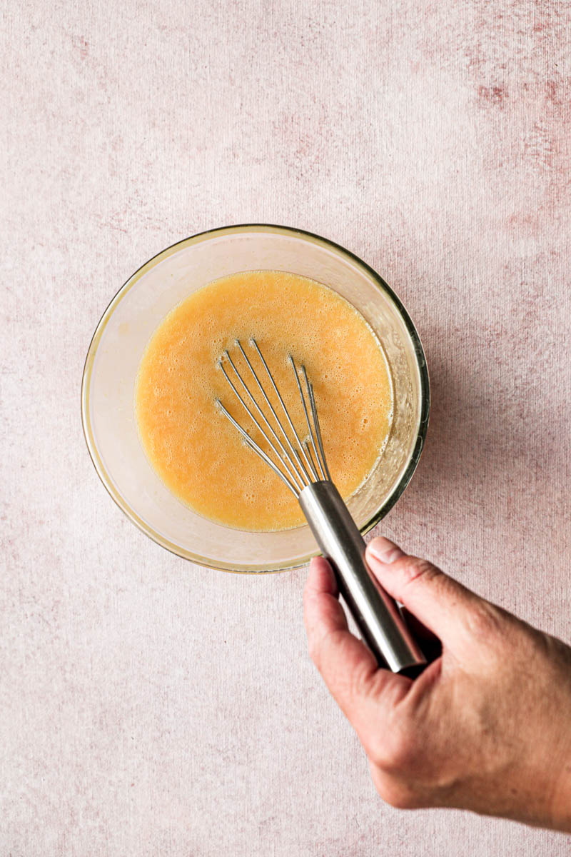 Making the lemon cream for the square lemon bars: a hand whisking the lemon juice/butter and the eggs/sugar/corn-starch.