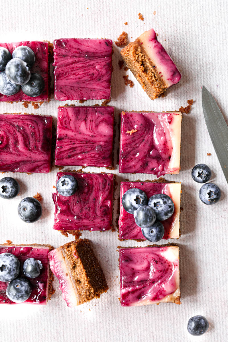 Overhead shot of all the blueberry lemon bars sliced into squares with a knife on the side over a pink backdrop.